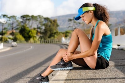 A runner sitting at the roadside holding her lower leg after an injury